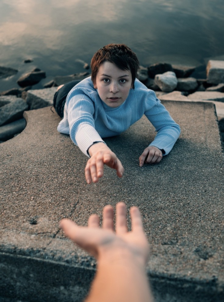 Woman falling off a ledge reaching out to a hand held out to help her.