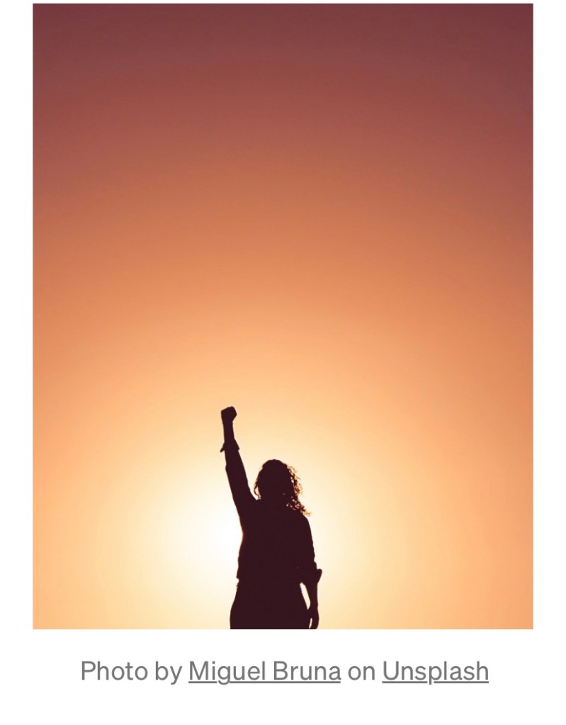A victorious woman holds her arm up in the air with a closed fist.