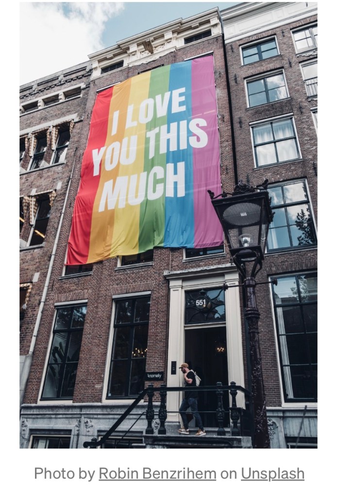 A gay pride flag flies above a brick building￼.
